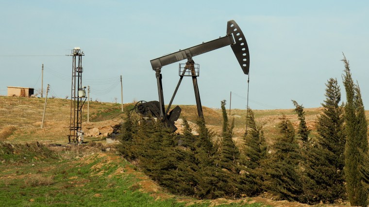 An oil pump jack rises above the horizon against a clear blue sky.