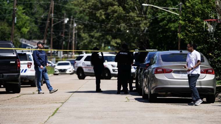 Yellow police tape stretched in front of law enforcement officials in a residential street.