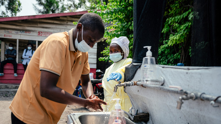 A visitor washes his hands at a sink operated by a hospital worker before entering Kyeshero Hospital 