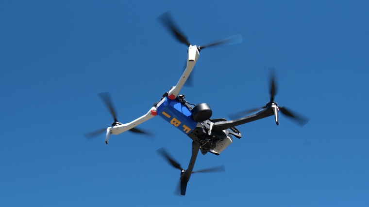 A blue and white drone hovering with FBI written on the bottom