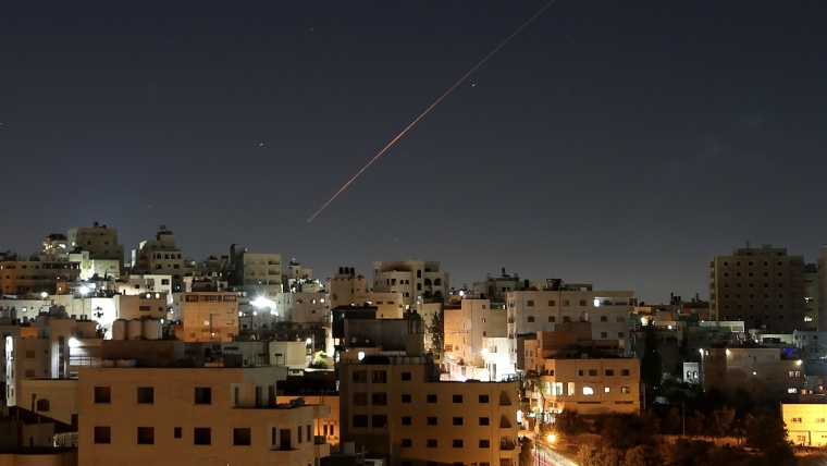 Streaks from a missile in the air over rooftops at night.