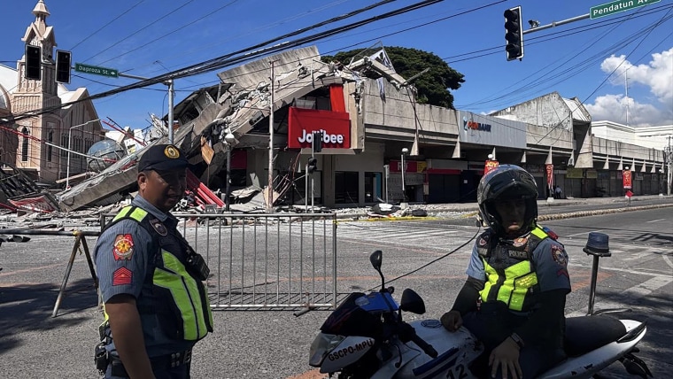 A severely damaged commercial building behind two police officers.