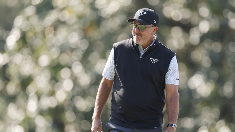 Phil Mickelson standing on a golf course wearing sunglasses against a blurred background.