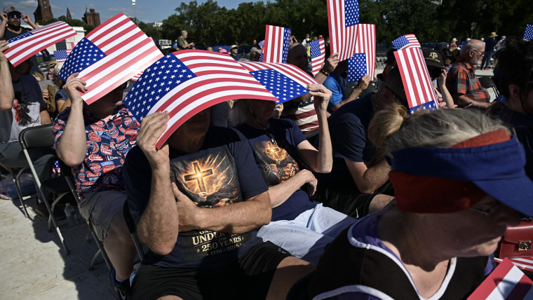 People sheltering from the sun under cardboard American flag signs.