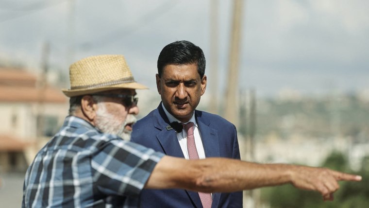 Ro Khanna listens as a pain with a brimmed hat speaks while pointing into the distance.