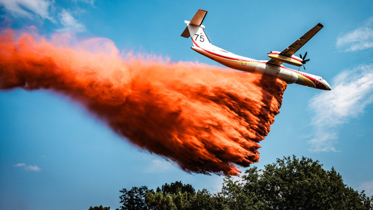 A Dash firefighting aircraft drops red fire retardant over a forest fire area