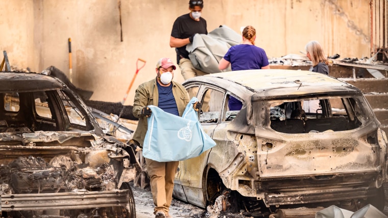 Residents carry the remains of deceased dogs at a home burned in the Old Trails fire in Spokane, Wash., on Aug. 4, 2026. 