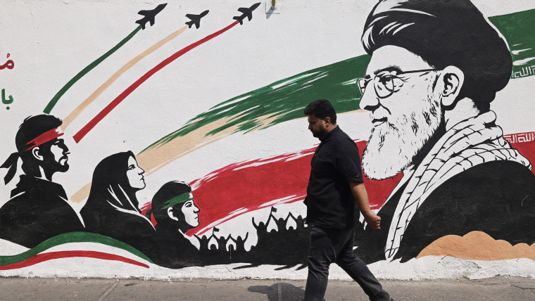 A man walks past a mural featuring Ayatollah Ali Khamenei on the street.
