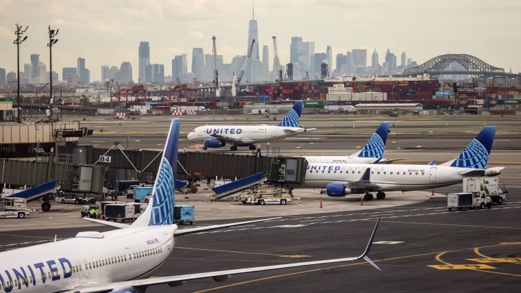 Four United Airlines jets sit on a tarmac with the New York City skyline visible in the distance.