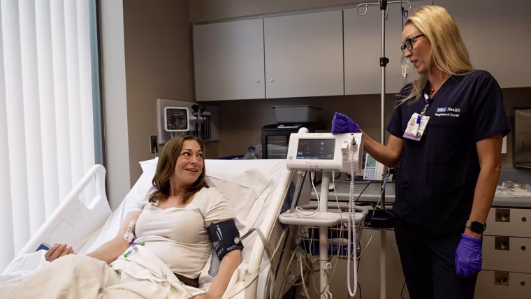 Image: Natalie Staubus in a hospital bed talking to a medical professional.