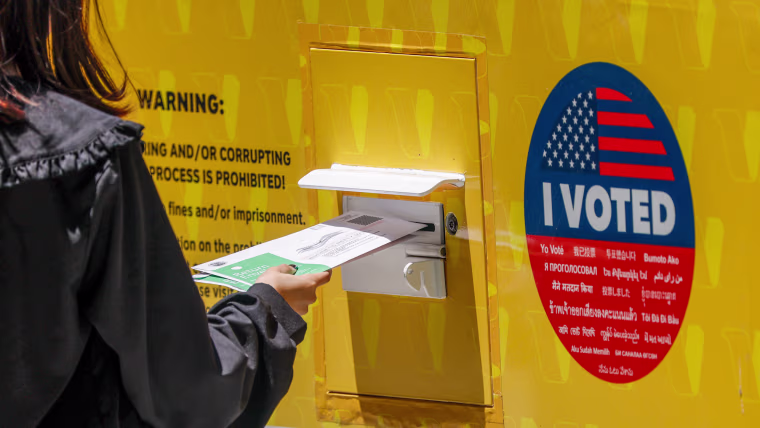 A person places their Mail in ballot into a ballot box.