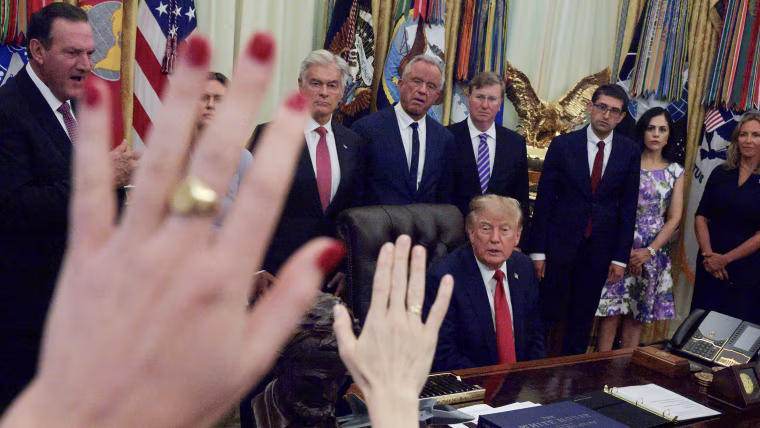 President Trump speaks to reporters while seated at his desk in the Oval Office and flanked by cabinet members.