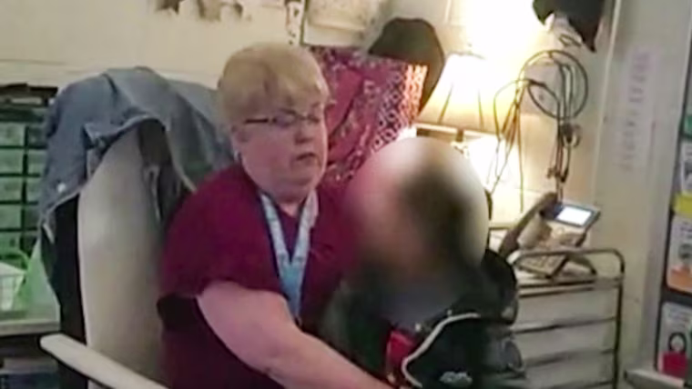 A child with their face blurred out is held by a teacher inside of a classroom