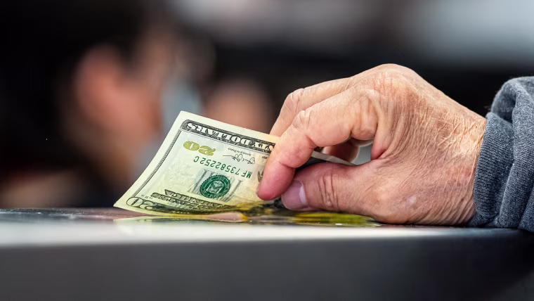 A hand resting on a counter top holds a 20 dollar bill