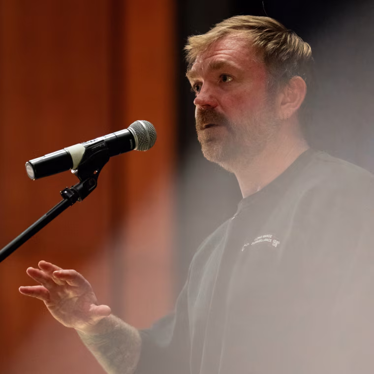 Graham Platner talks into a standing microphone on stage