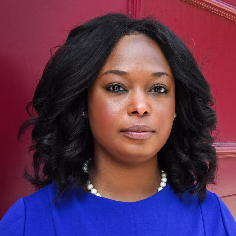 Janeese Lewis George stands for a portrait in front of a red background