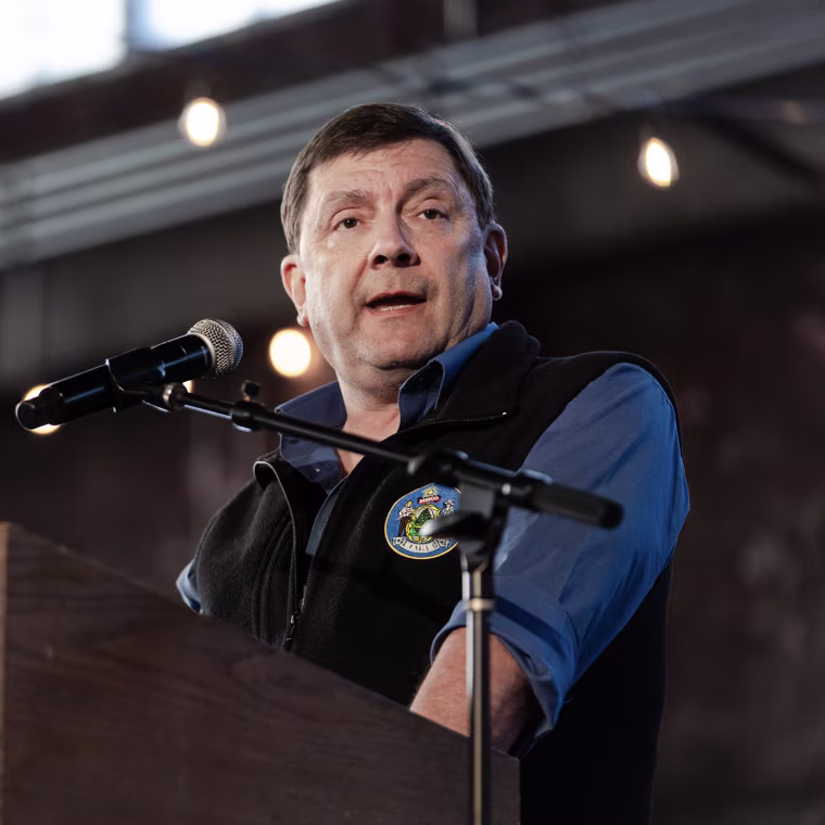 Troy Jackson speaking at a lectern with a sign reading FIGHT OLIGARCHY.
