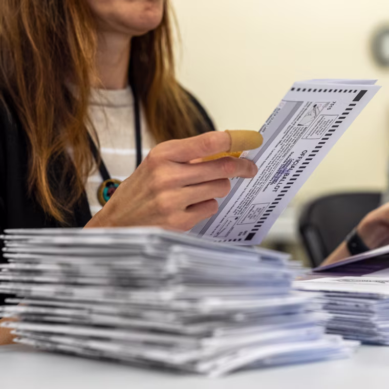 A woman extracts a mail-in ballot from an envelope.