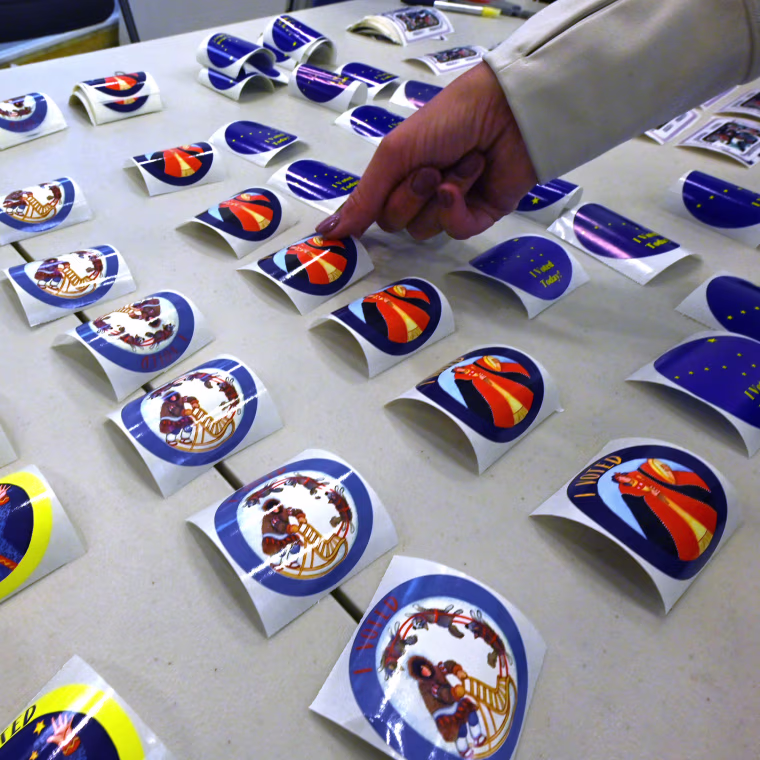A person grabs a "I Voted" sticker from a table.