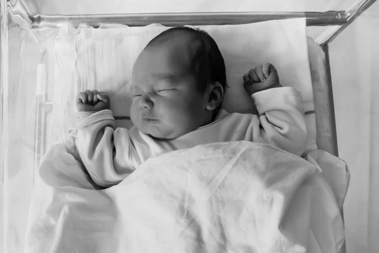 Newborn baby is sleeping in small transparent portable plastic bed.