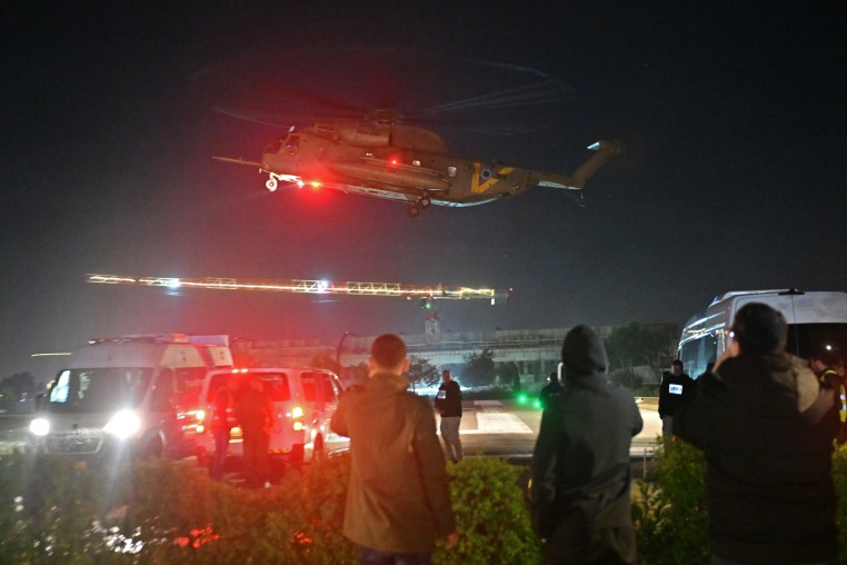 People wait at a helipad as a helicopter carrying released hostages lands