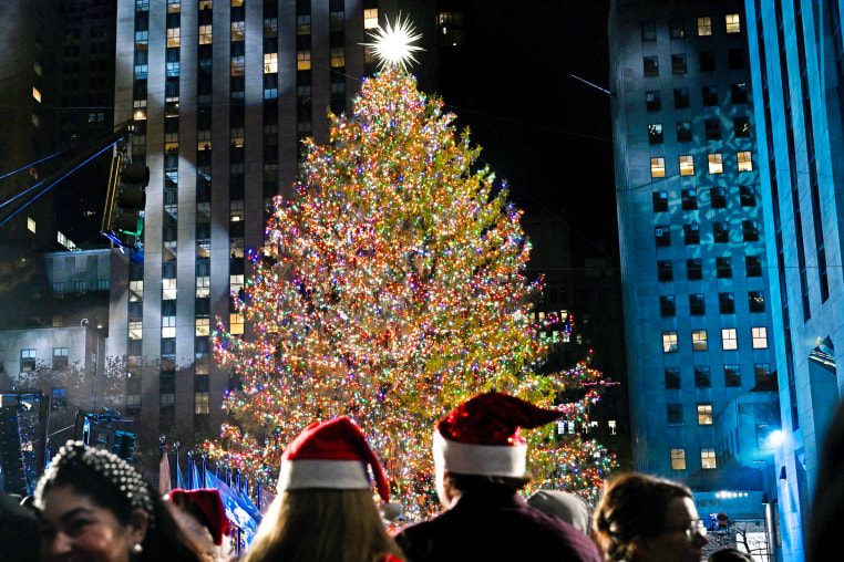 People in christmas hats look at the Rockefeller Christmas tree lighting in a crowd.