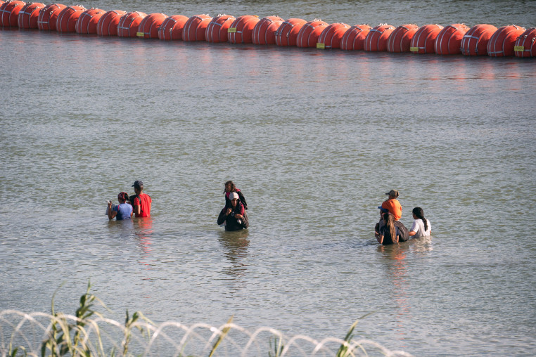 Image: Asylum-seeking migrants walk in the Rio Grande river between the floating fence 