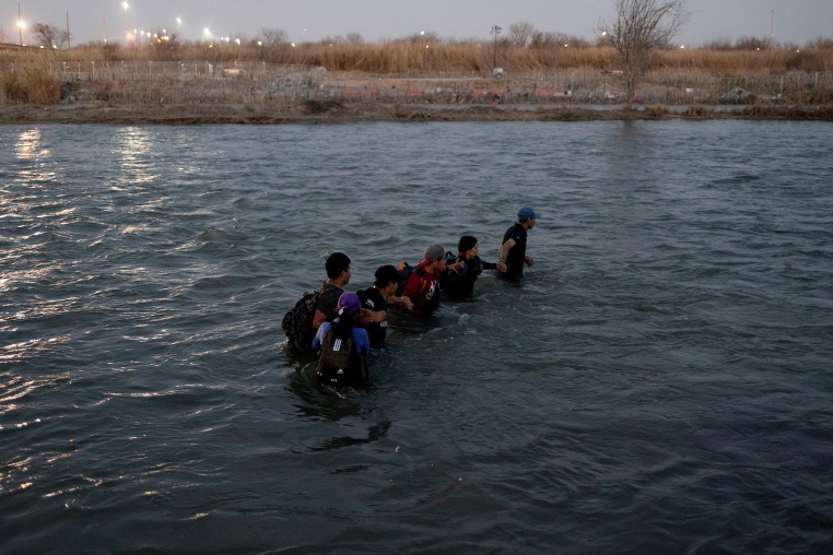 Migrants hold hands as they cross the Rio Grande.