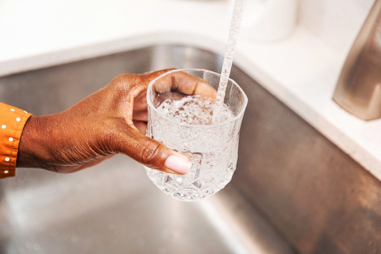 Woman pouring herself a glass of tap water from the kitchen sink