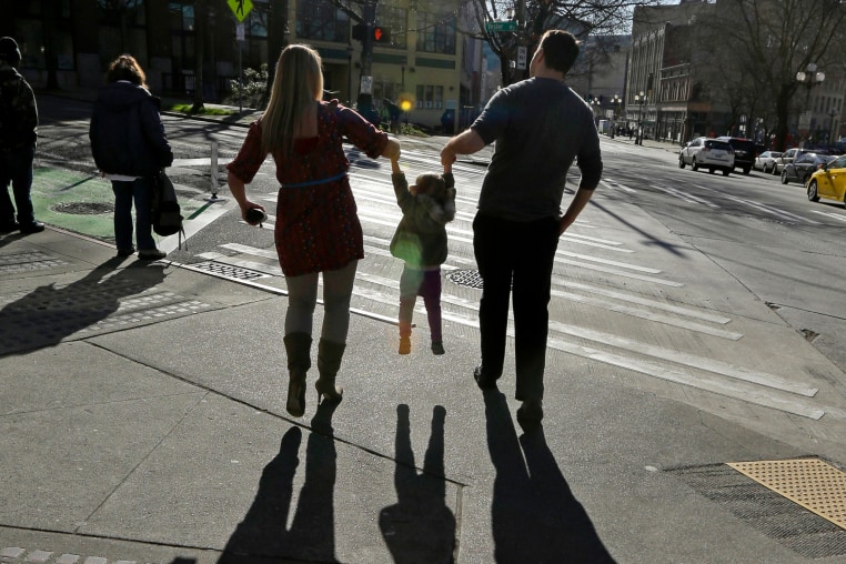 A child is lifted by her parents at a street corner in downtown Seattle.