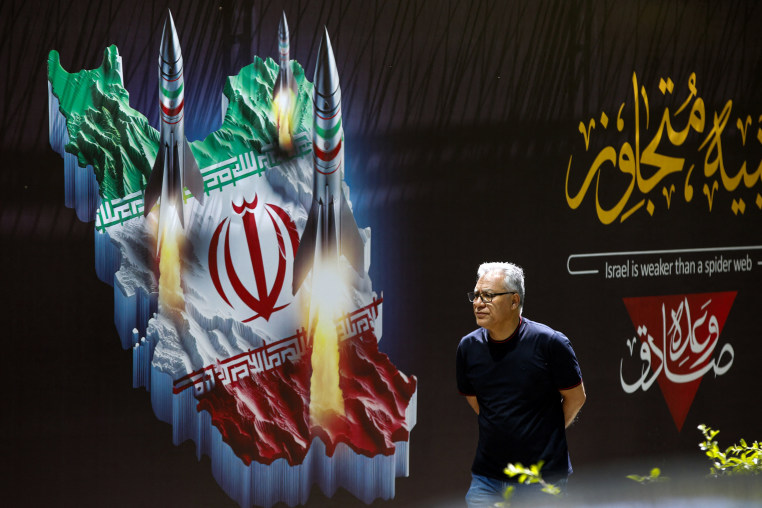 A man walks past a banner depicting missiles along a street in Tehran 