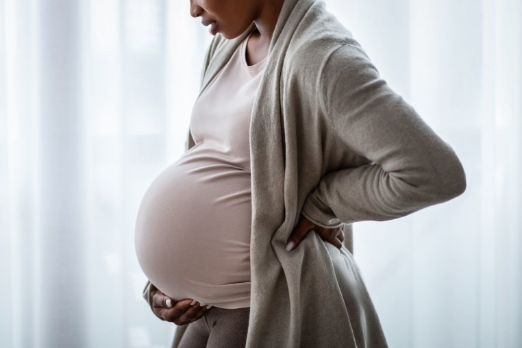 Side pregnant black woman standing next to window