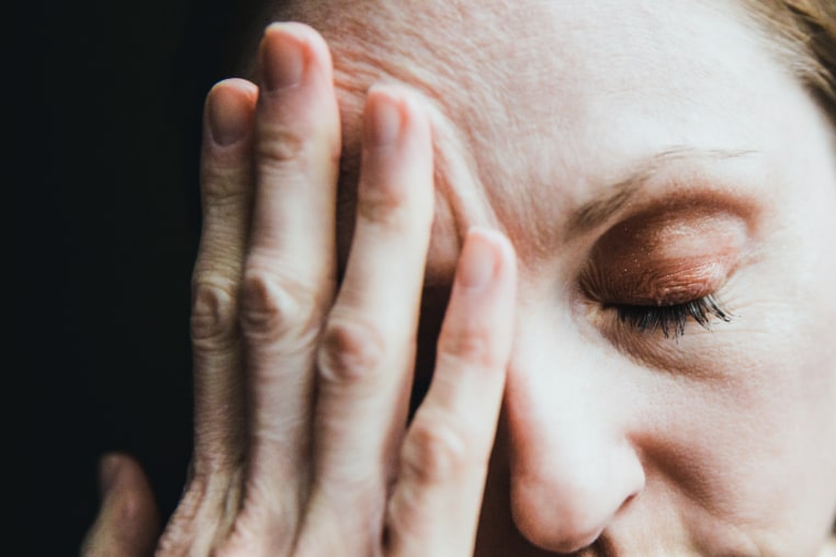 A woman with a migraine, hand over forehead in pain
