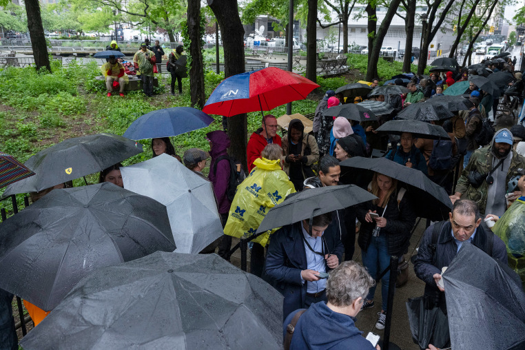 People hold umbrellas as they wait in line in the rain 