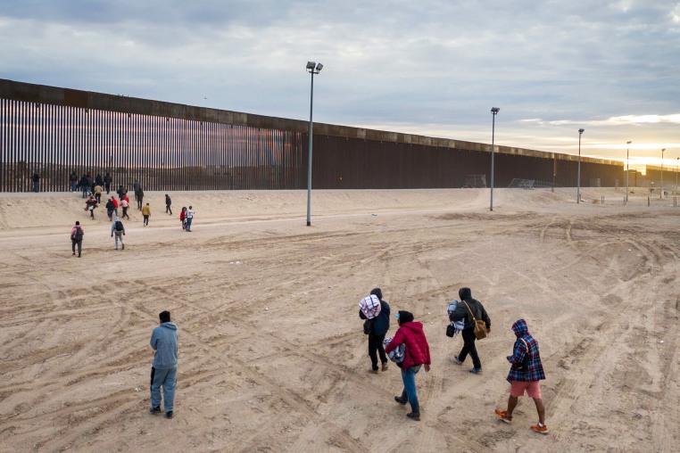 Group of immigrants walk toward the border wall. 