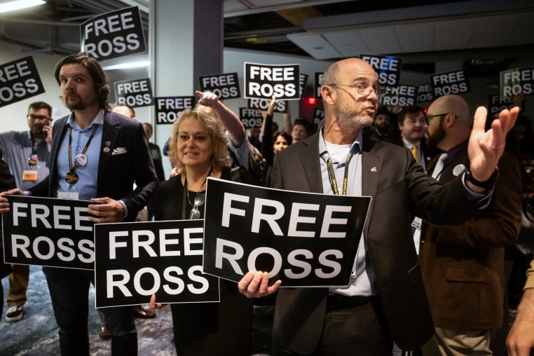 Libertarian Party delegates wait to enter a ballroom for a speech by former President Donald Trump holding signs that say "Free Ross"