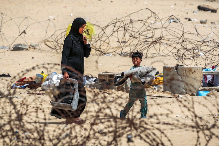 A woman and boy walk with belongings past barbed-wire fences as they flee from Rafah 
