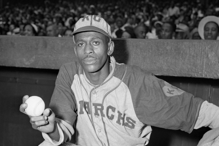 Pitcher Satchel Paige stands at the top of the dugout with baseball in hand