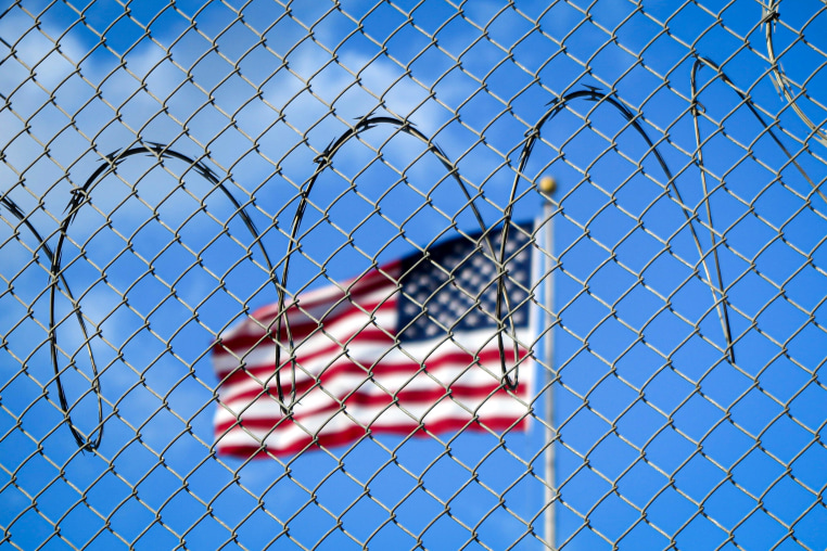 A U.S. flag flies behind barbed wire.