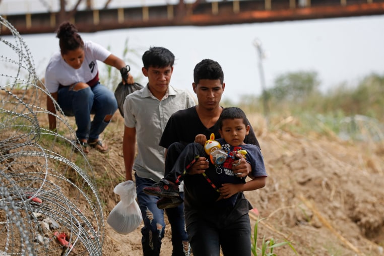 Migrants walk past razor wire fencing after crossing the Rio Grande river in Eagle Pass, Texas 