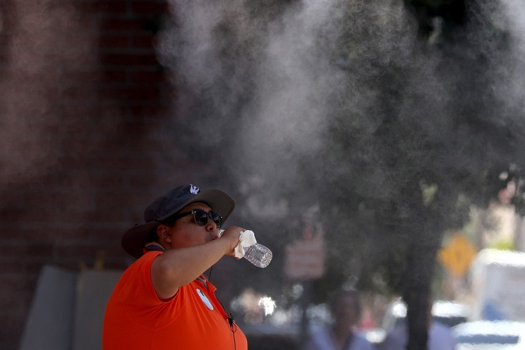 A Downtown Phoenix Ambassador takes a drink of water while cooling off under a mister in Phoenix