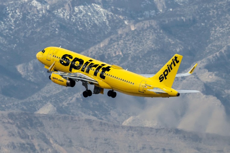 A Spirit Airlines plane flies near a mountain scape
