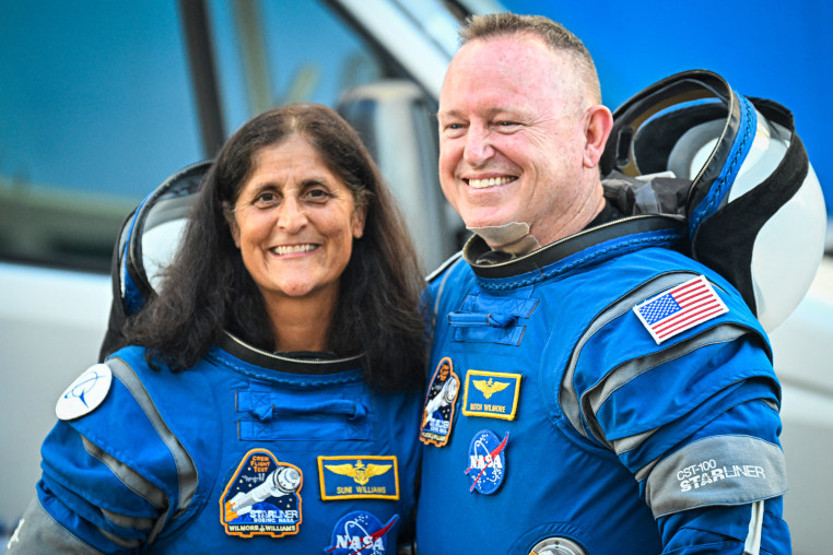 Suni William and Butch Wilmore stand and smile for a photo together in their Boeing space suits