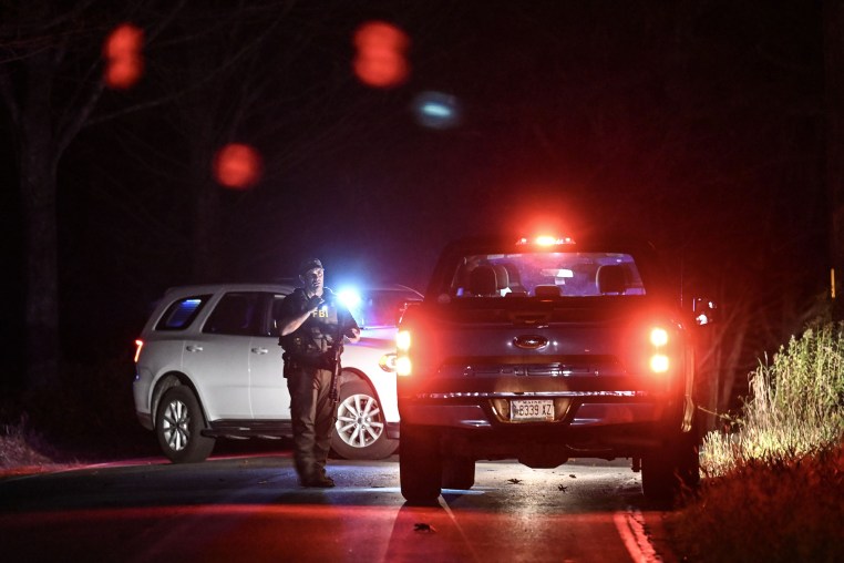 An armed police officer stands on the road with emergency vehicles