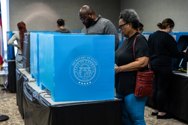 Voters cast their ballots inside of a room at tables with blue dividers