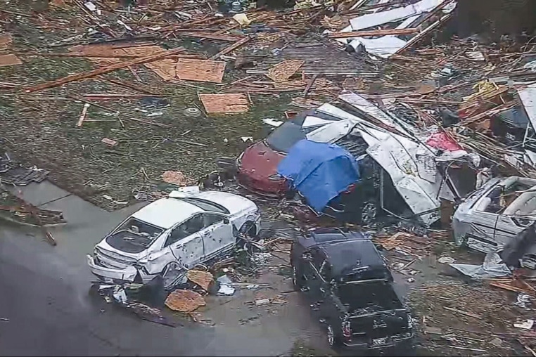 An aerial view of damaged cars surrounded by debris on the road and a lawn