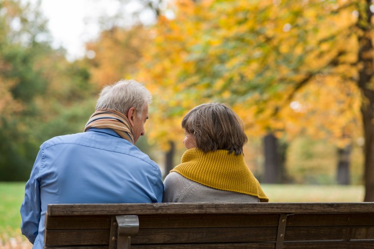 Rear view on Senior couple sitting on park bench in autumn