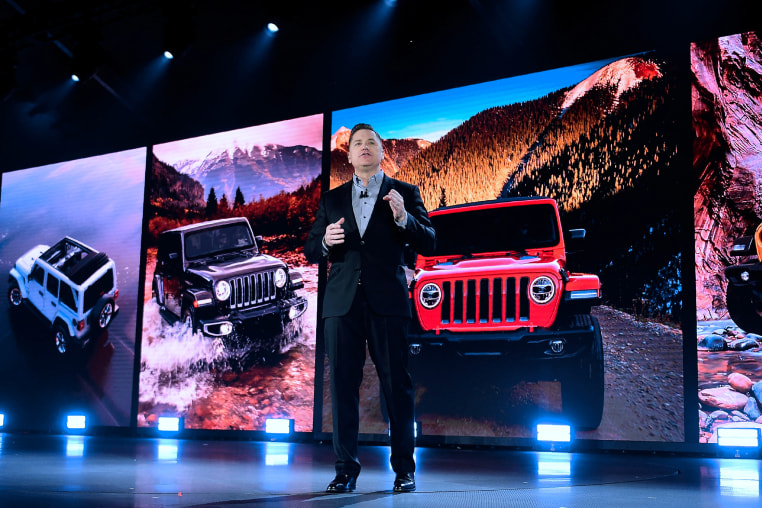 Tim Kuniskis stands in front of images of the new cars