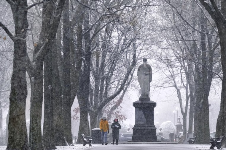 Image: Snow falls as a couple walks along the Commonwealth Avenue Mall in the Back Bay neighborhood of Boston on Dec. 20, 2024.