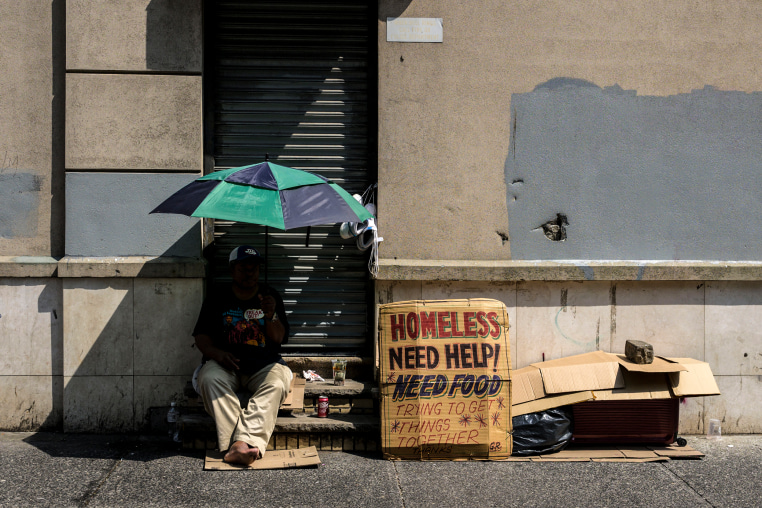 A homeless person holds an umbrella to block out the sun